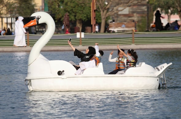 Woman takes a selfie with her children as they ride a boat at Aspire Park in Doha